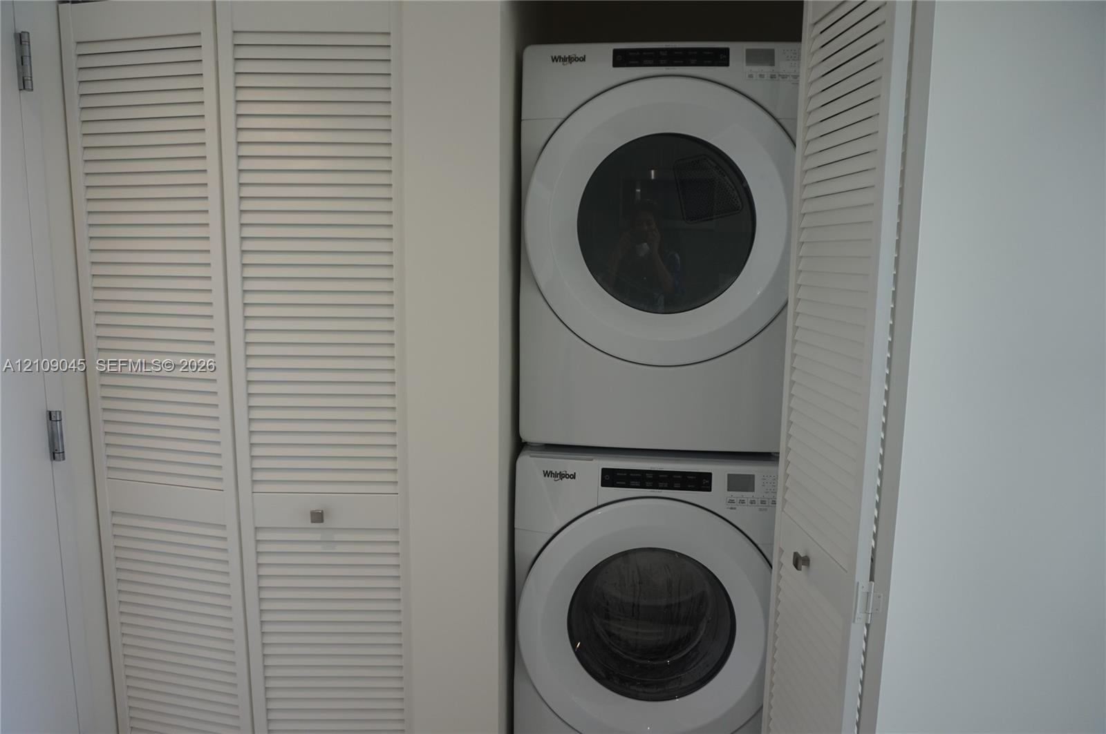 Stacked laundry center featuring a white Whirlpool front-load washer and dryer enclosed by white louvered bifold doors
