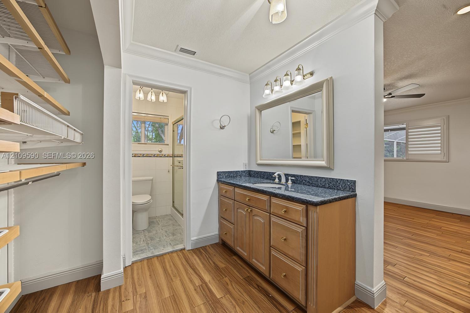 Bathroom vanity area featuring a stone-topped cabinet, framed wall mirror, multi-bulb vanity lighting, and open-shelf storage