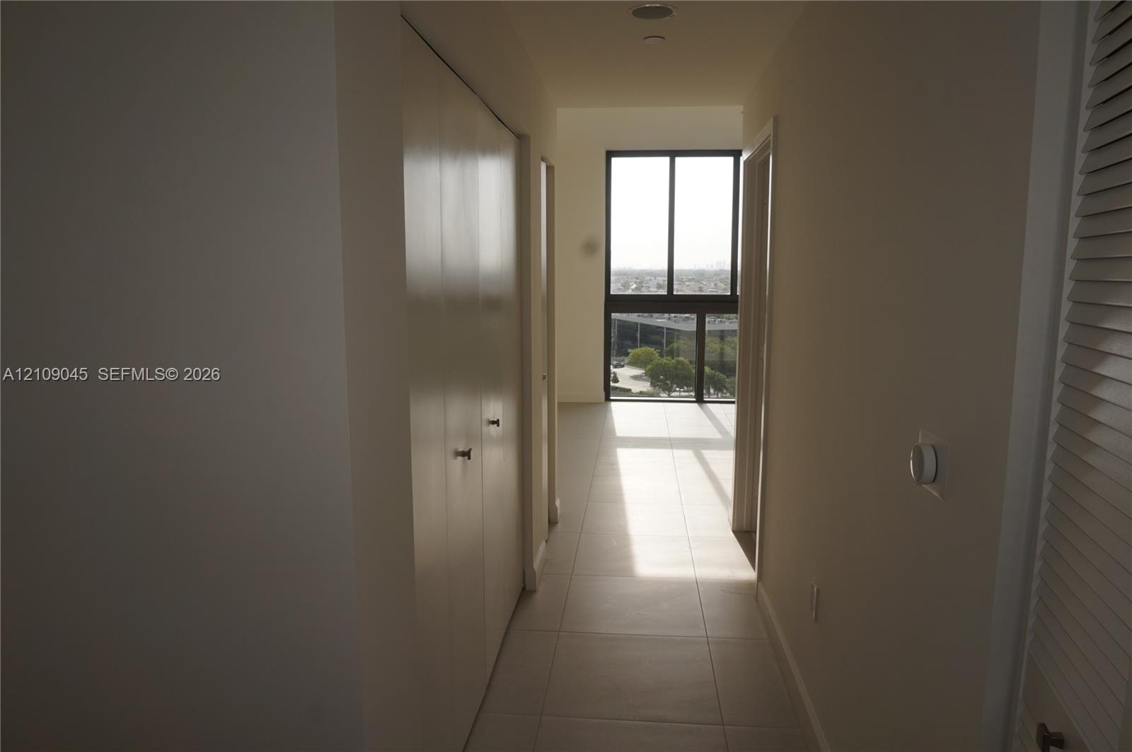 Hallway featuring large-format floor tile, double-door closet, and floor-to-ceiling windows