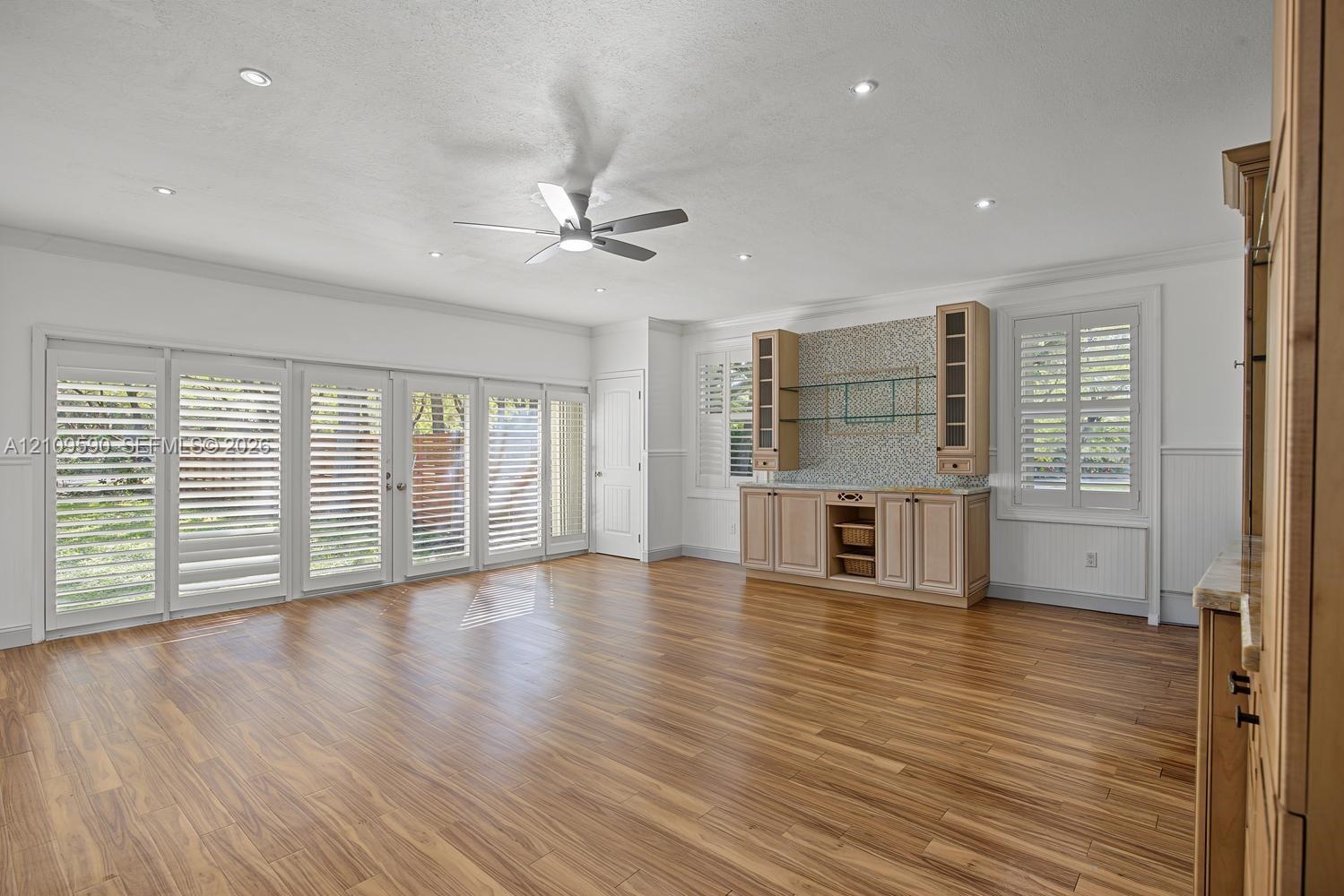 Living area featuring wood-finish flooring, recessed lighting, a ceiling fan, a set of multi-panel sliding doors with integrated shutters, and built-i