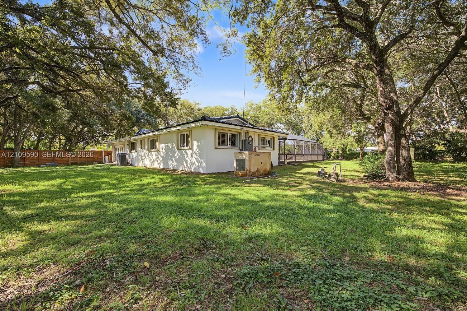 Expansive backyard featuring mature shade trees, a screen-enclosed patio, and a wood-slat perimeter fence