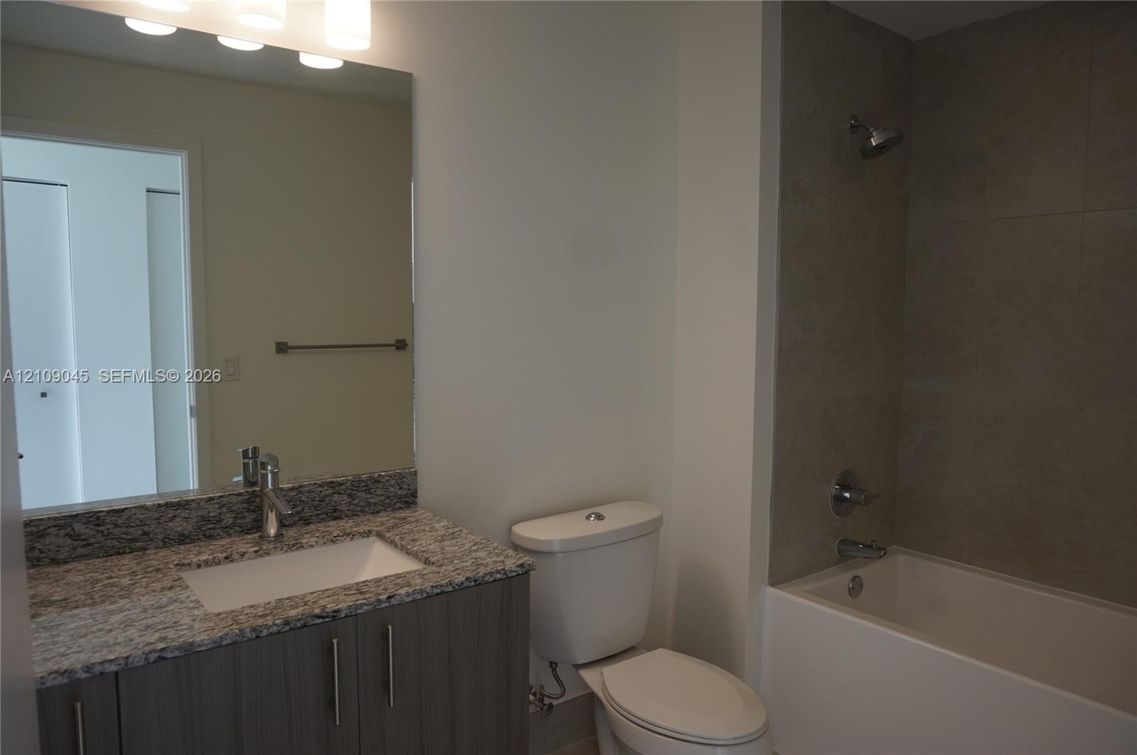 Bathroom featuring a stone-top vanity with an undermount sink, large wall-mounted mirror, brushed-nickel hardware, and a tub with a floor-to-ceiling t