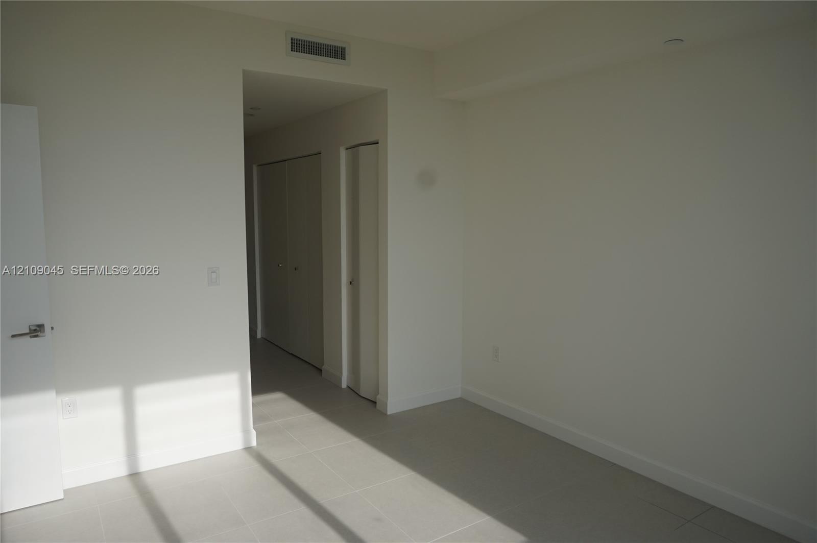 Neutral interior space featuring large-format ceramic floor tiles, recessed ceiling lighting, and multiple reach-in closets with doors