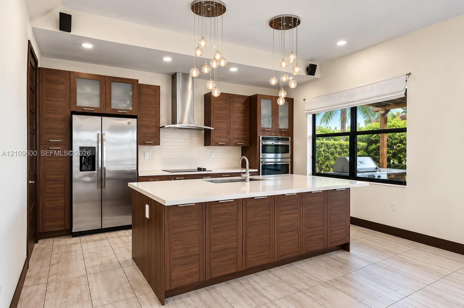 Kitchen featuring dark wood-finish cabinetry, a quartz-topped center island with integrated sink, stainless steel appliances, tiered glass globe penda