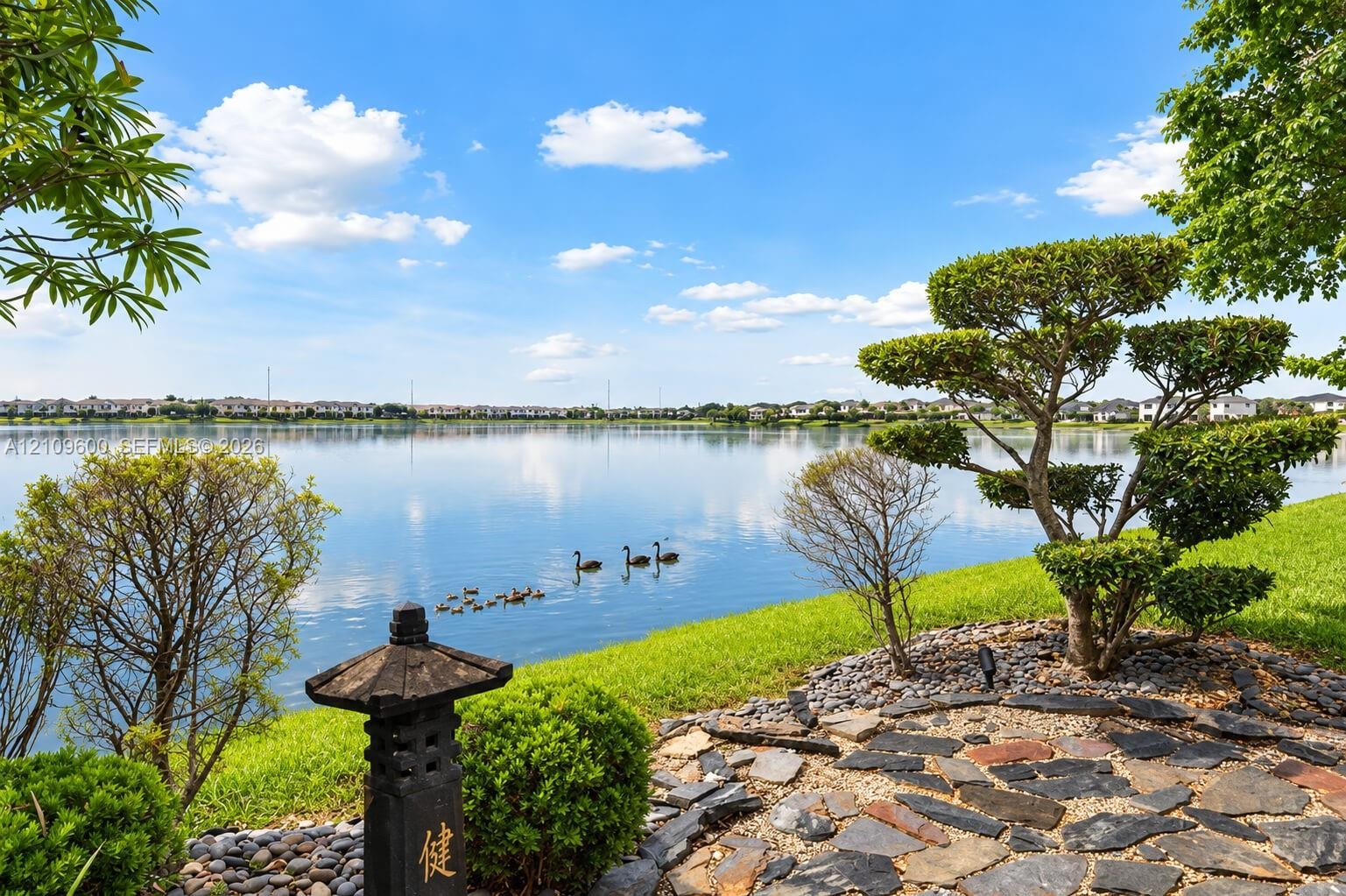 Waterfront property featuring a stone paver terrace, manicured lawn, tiered topiary landscaping, and a decorative stone lantern