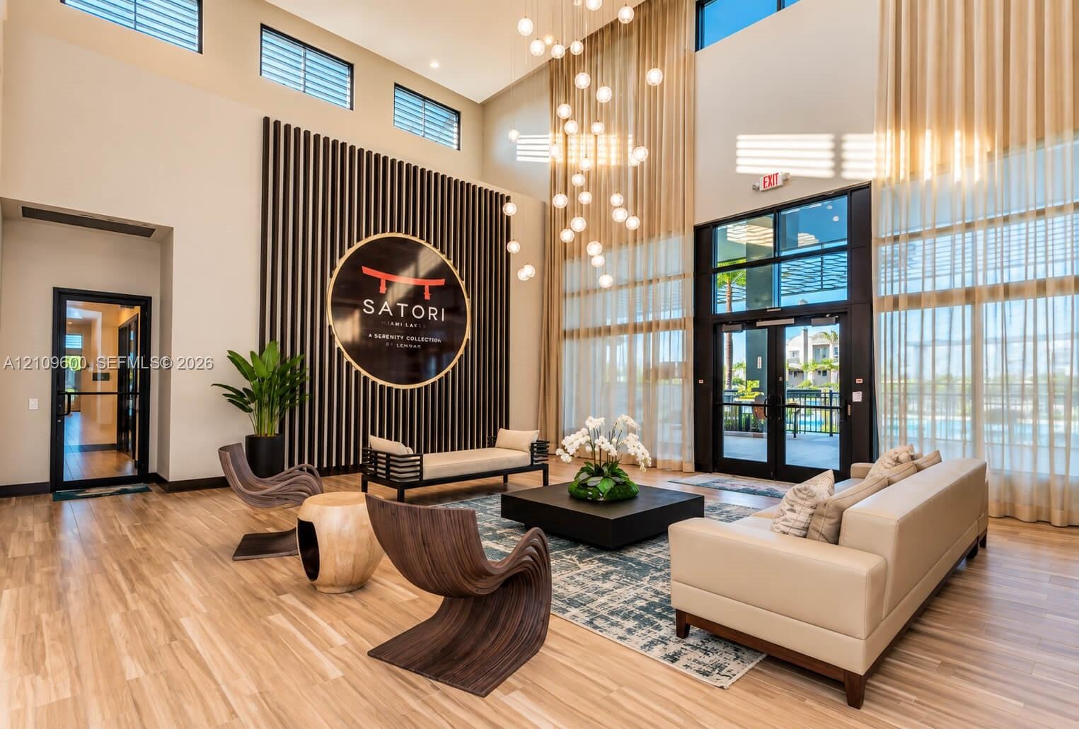 Double-height ceilings featuring floor-to-ceiling windows, wood-finish flooring, vertical slat accent wall, and a multi-tiered modern chandelier