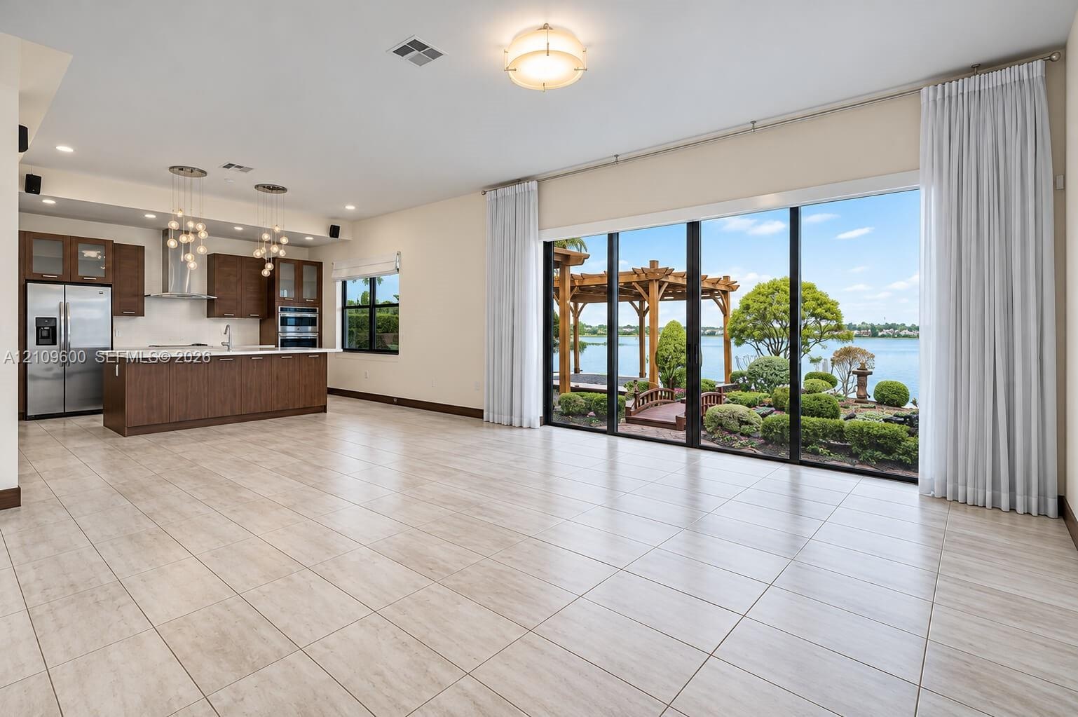 Open-concept living space featuring large-format tile flooring, a kitchen with dark-finish cabinetry, built-in stainless steel appliances, tiered pend