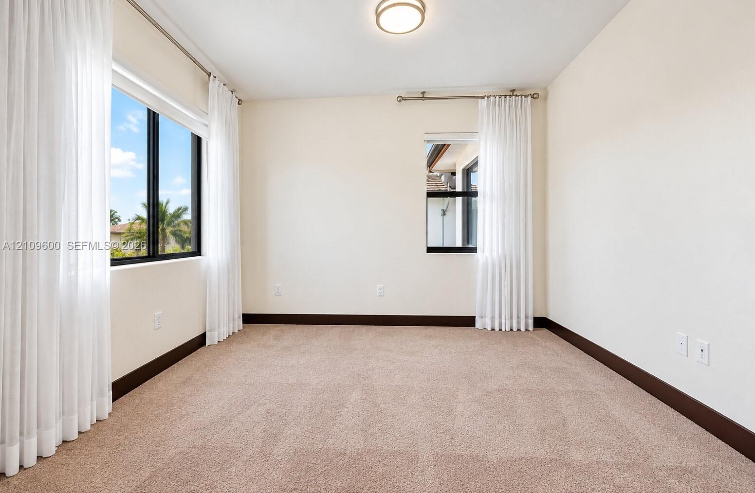 Neutral wall-to-wall carpeting, dual black-framed windows, and a flush-mount overhead light fixture