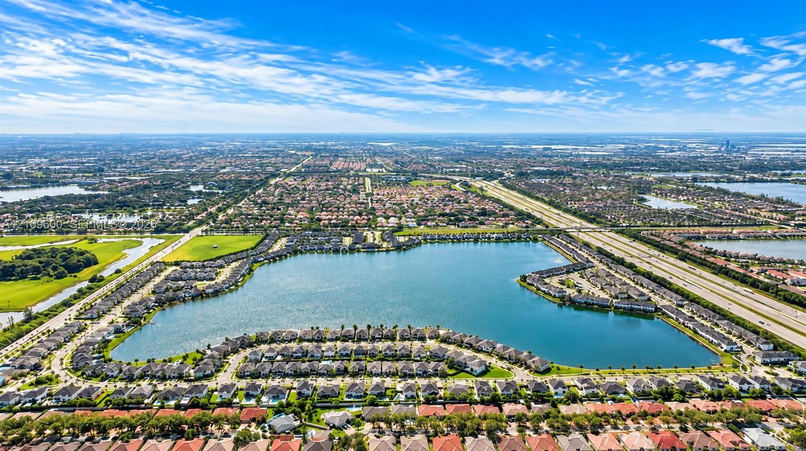 Aerial perspective of a master-planned community encompassing a central lake, expansive waterfront residential lots, integrated street network, and pr