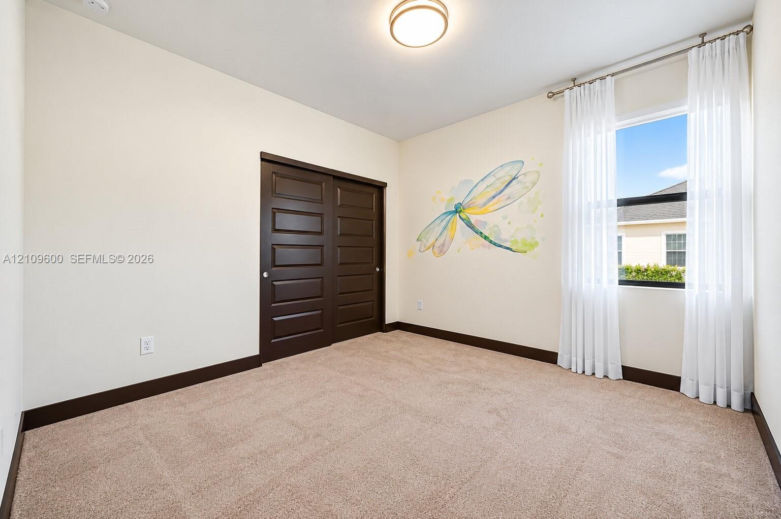 Neutral-toned carpeted room featuring dark-finished sliding closet doors, a flush-mount ceiling light, and a single window with curtain rod hardware