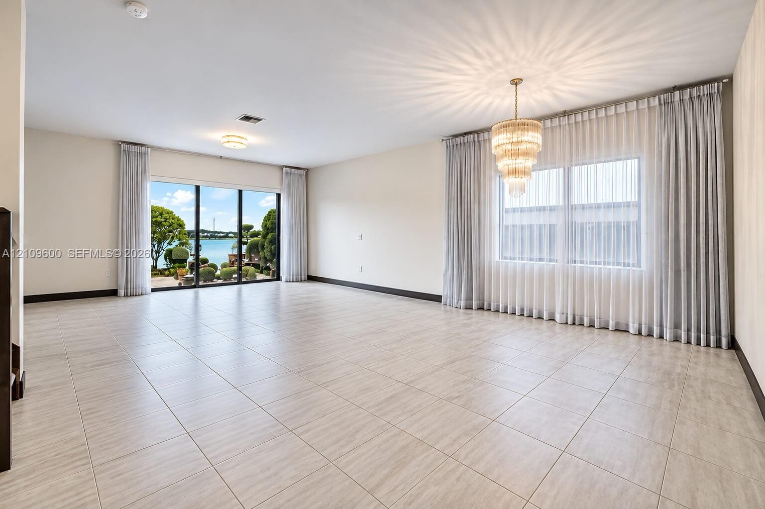 Spacious interior featuring large-format tile flooring, multi-tiered crystal chandelier, and floor-to-ceiling glass sliding doors