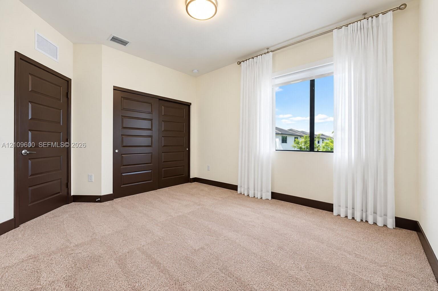 Neutral wall tones, wall-to-wall carpeting, sliding closet doors with dark wood-finish, matching dark wood-finish interior door, and a single-pane win