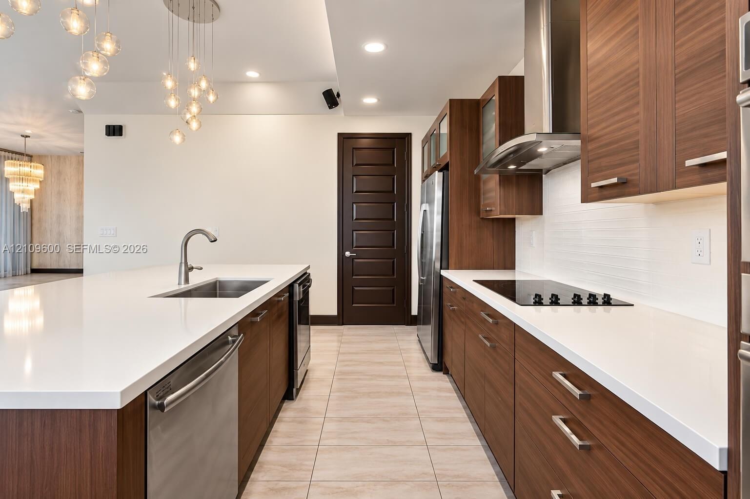 Modern kitchen featuring flat-panel wood-finish cabinetry, white quartz countertops, stainless steel appliances, and multi-light pendant fixtures