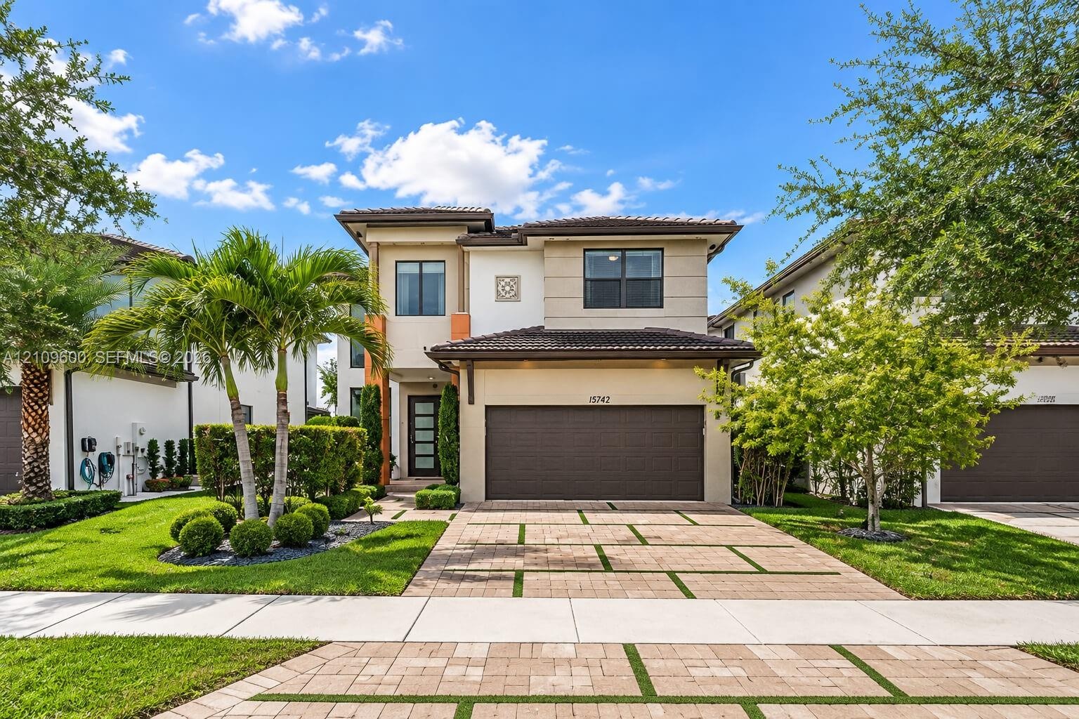 Two-story exterior featuring a contemporary facade, multi-tonal stucco finish, tile roof, multi-car garage, and a paver driveway with turf accents