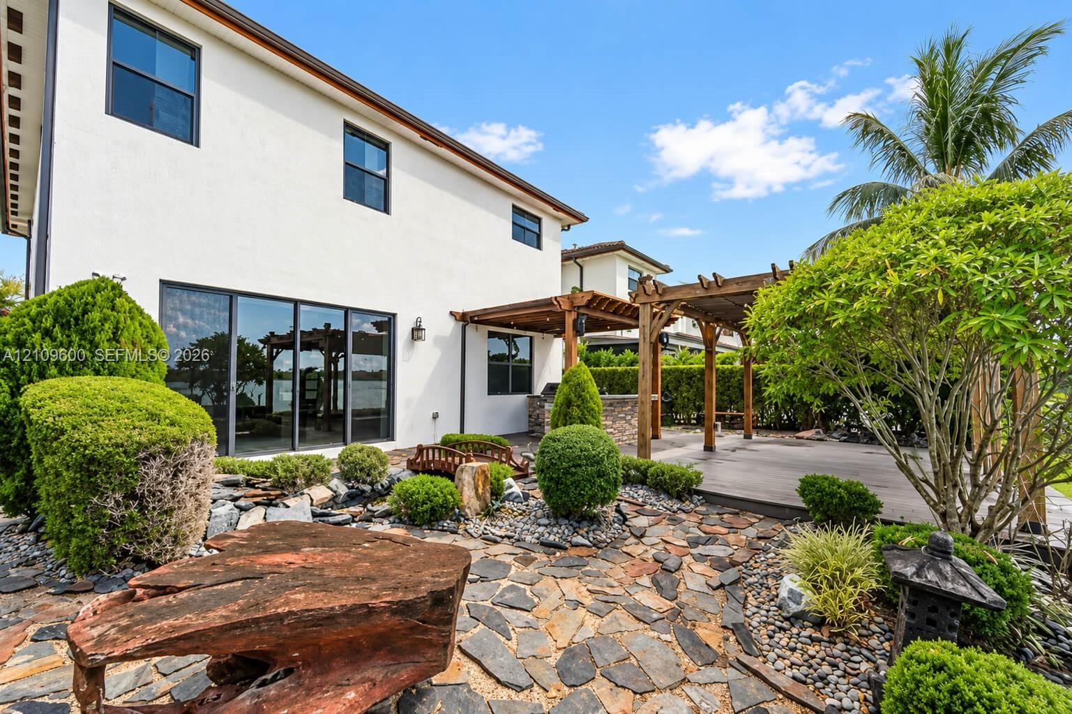 Stucco exterior featuring a wood-beam pergola, stone-paved patio, custom rock garden landscaping, and sliding glass doors