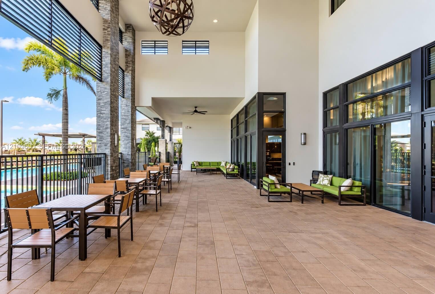 Covered outdoor patio featuring tile flooring, stone-accented support columns, expansive floor-to-ceiling glass panel walls, and a geometric pendant l