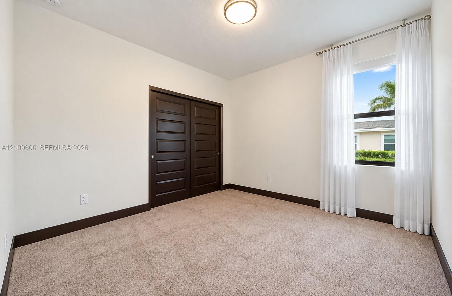 Neutral-toned carpeted flooring, dark-finish paneled closet doors, contrasting dark trim, and a flush-mount ceiling fixture