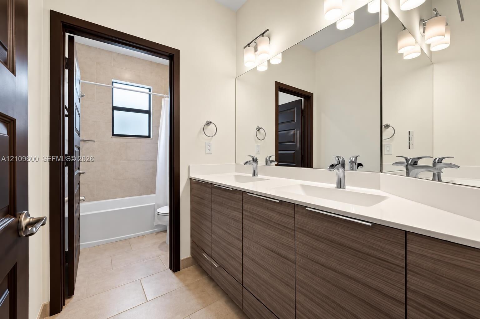 Double vanity featuring flat-panel cabinetry, light-toned stone countertops with integrated rectangular sinks, wall-to-wall mirror, and dual chrome fa
