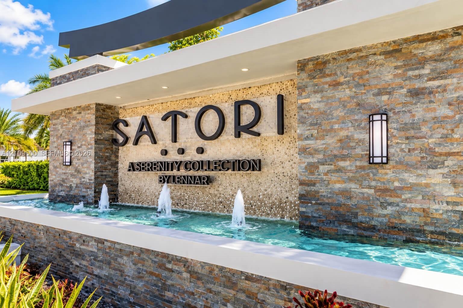 Community entrance featuring tiered stacked stone masonry, a multi-jet water feature, professional landscape lighting, and structural concrete framing
