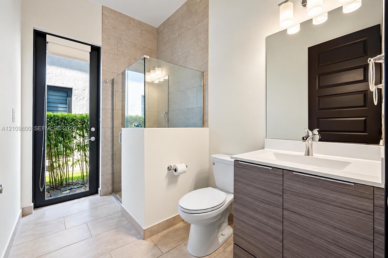Bathroom featuring a floating vanity with a wood-finish cabinet and solid-surface countertop, a glass-enclosed walk-in shower with neutral tile surrou