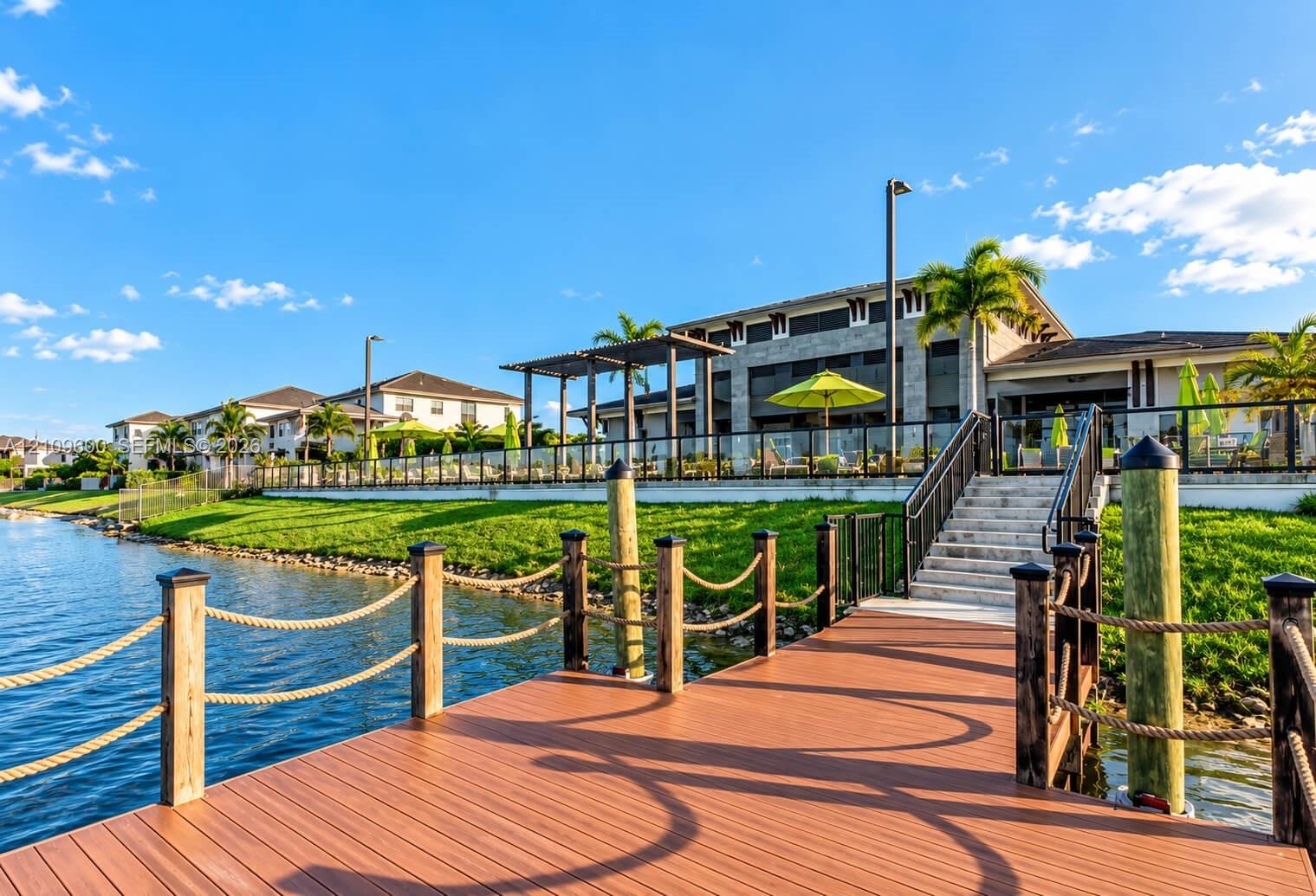 Private dock featuring composite decking, timber pilings with rope railing, and stone steps leading to an elevated patio with glass balustrade