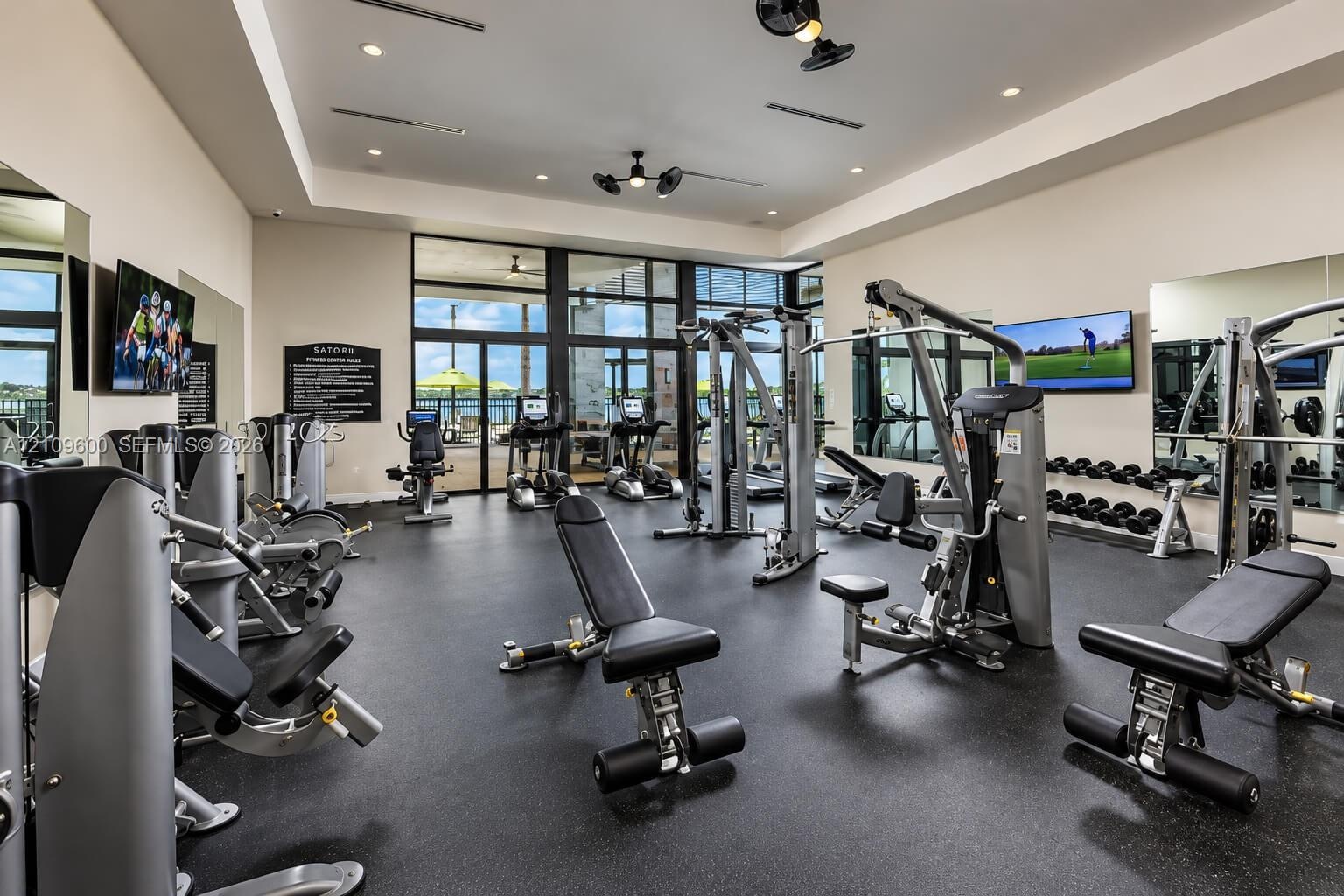 Fitness center featuring rubber flooring, recessed lighting, ceiling fans, full-height wall mirrors, and expansive floor-to-ceiling glass paneling