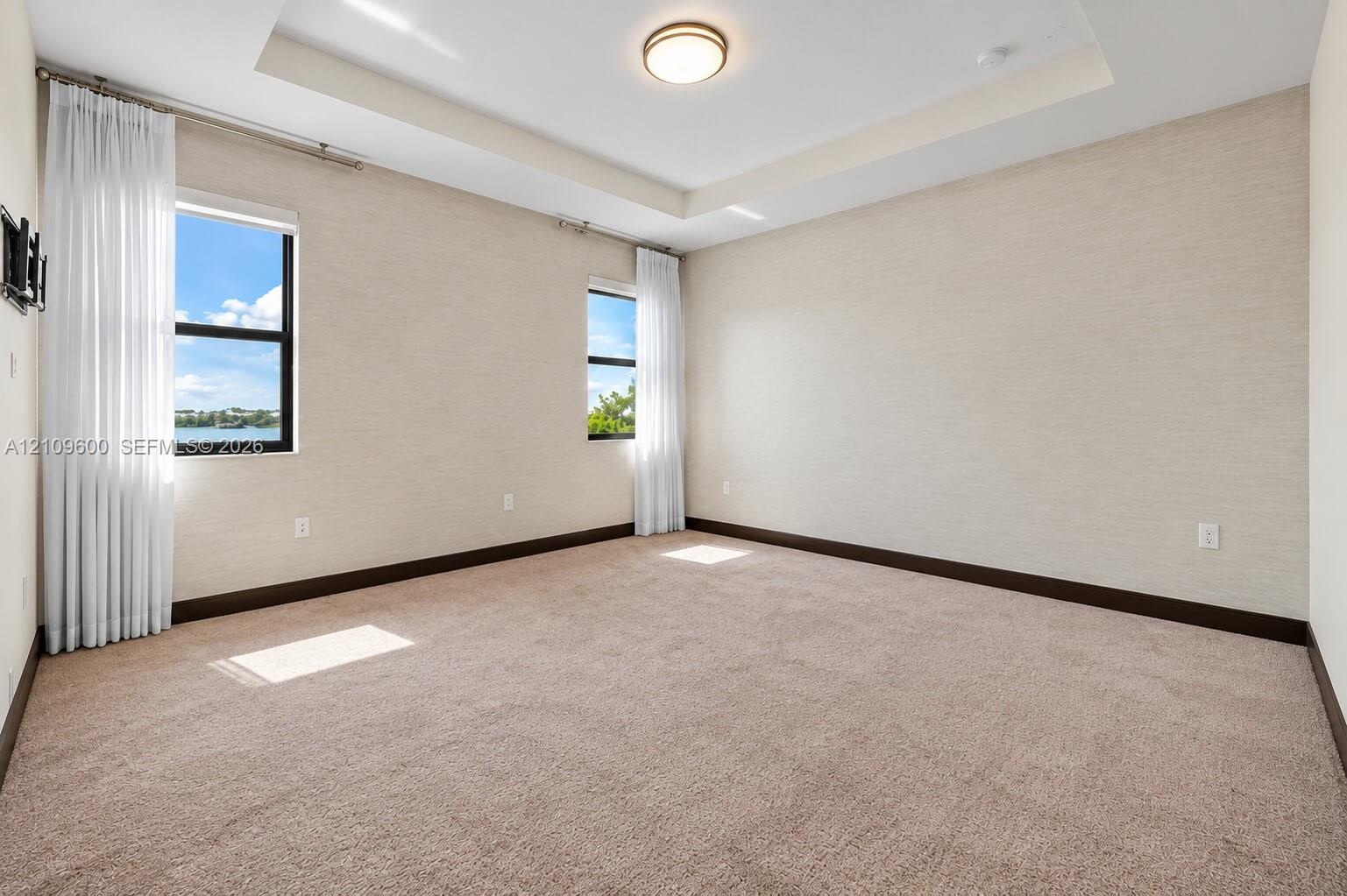 Neutral-toned wall coverings, tray ceiling, flush-mount lighting, wall-to-wall carpeting, and dual windows
