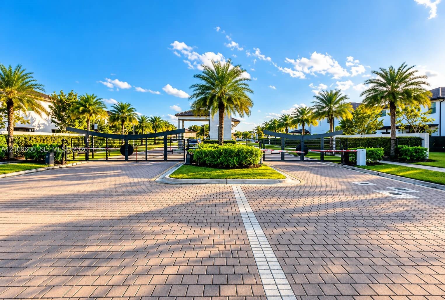 Gated entry featuring a paver driveway, metal security gates, and manicured landscaping with palm trees