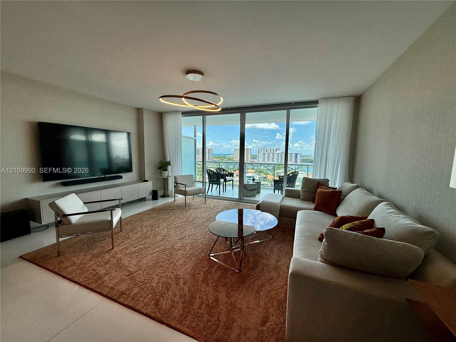 Living area featuring floor-to-ceiling glass sliding doors, built-in wall-mounted cabinetry, polished tile flooring, and a modern circular LED pendant