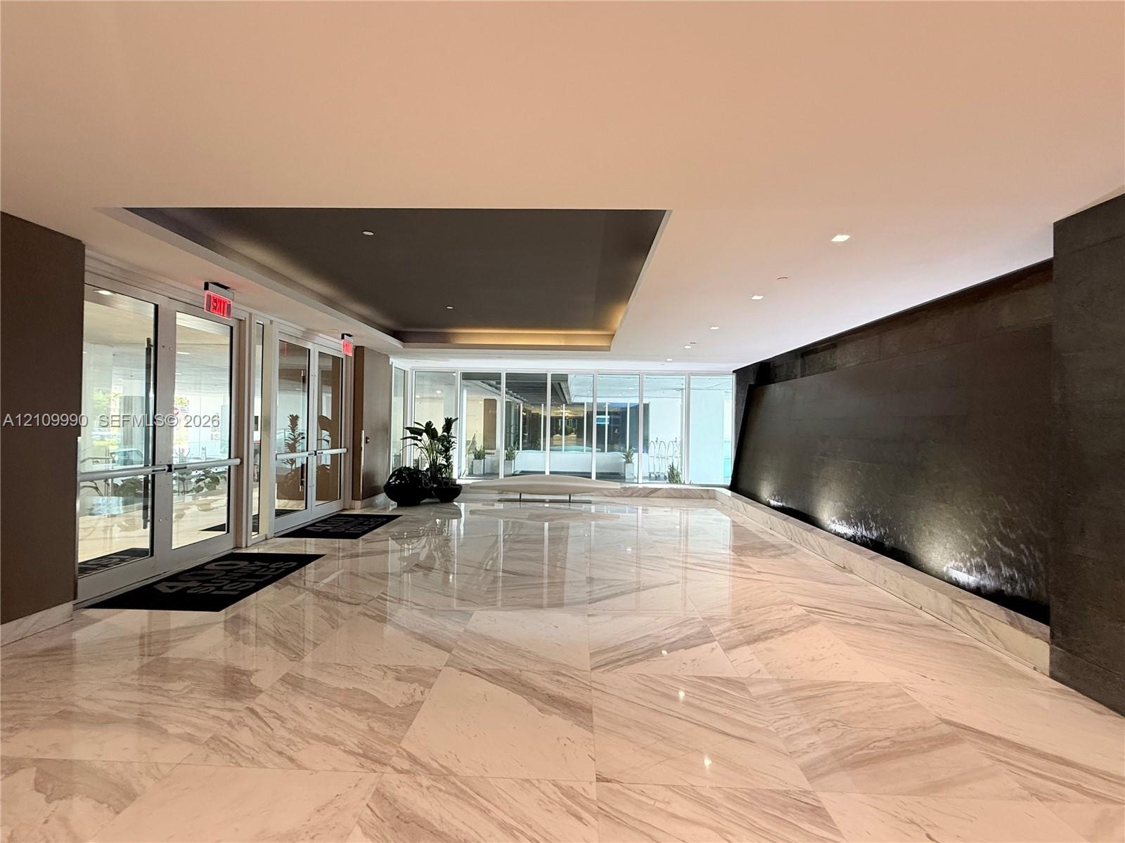 Spacious lobby featuring polished stone flooring in a geometric pattern, an expansive dark-toned accent water wall, recessed ceiling detailing, and gl