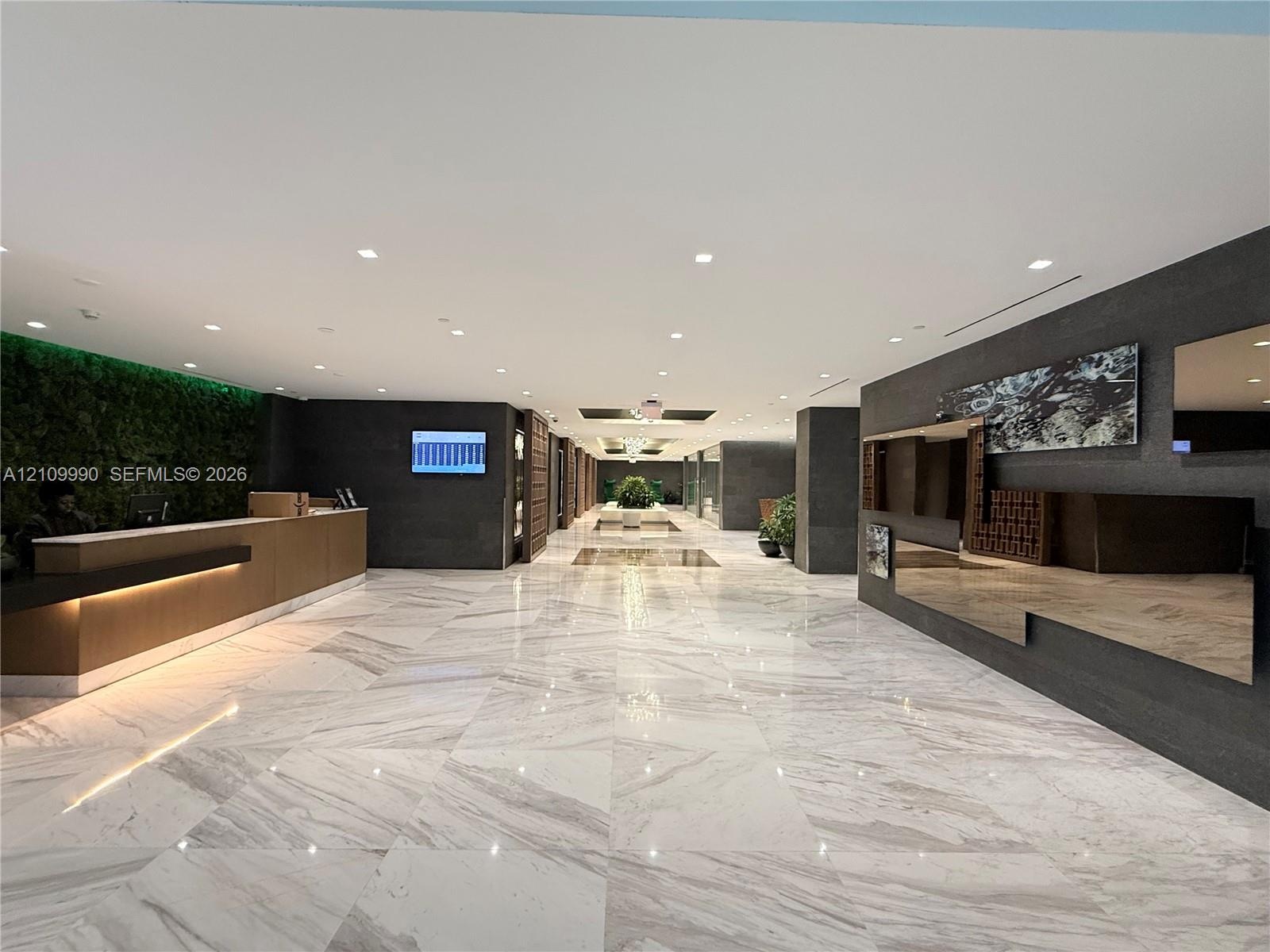 Lobby interior featuring large-format polished stone flooring, a built-in reception desk with integrated under-counter lighting, a full-height living 