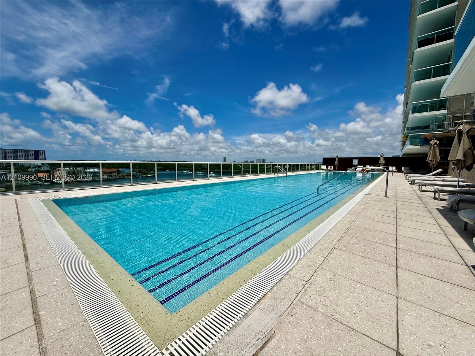 Rooftop swimming pool featuring a lap-style design, light-toned stone decking, and a glass perimeter railing