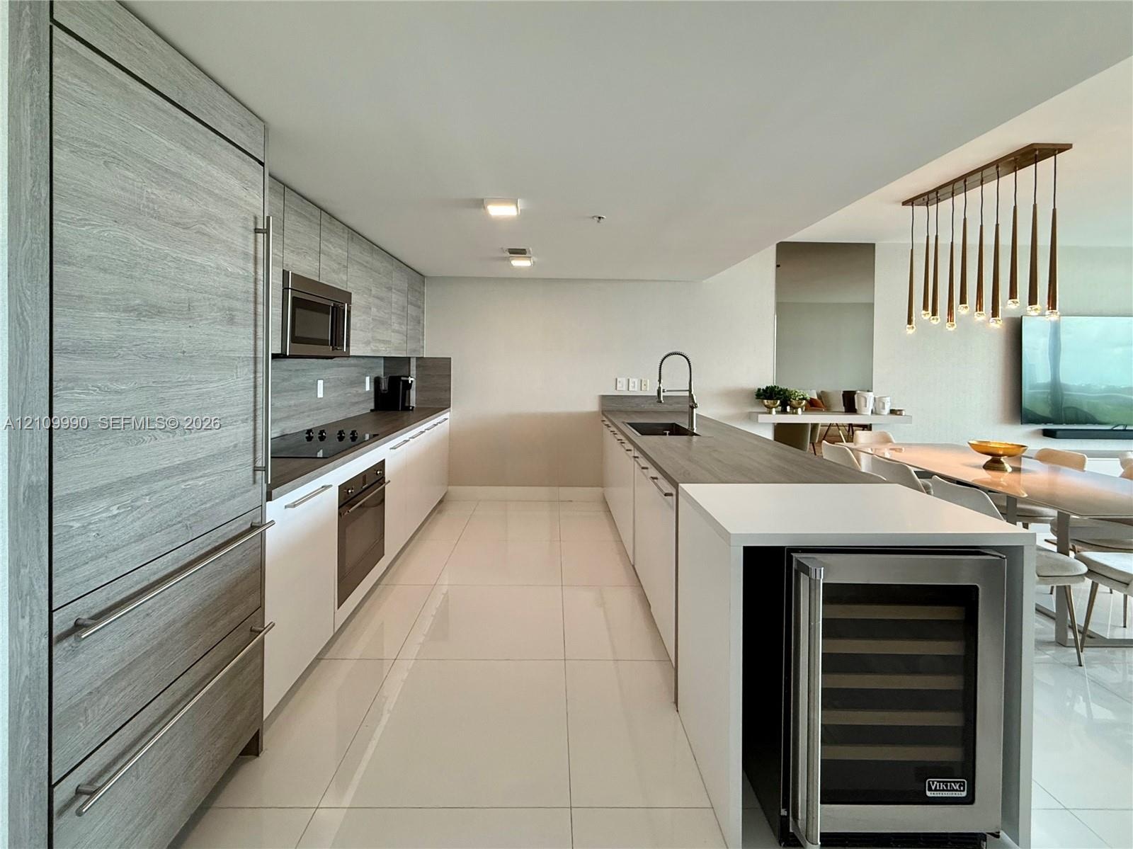 Kitchen featuring flat-panel wood-finish cabinetry, stainless steel built-in refrigerator, integrated wine cooler, stone-surface countertops, and mult
