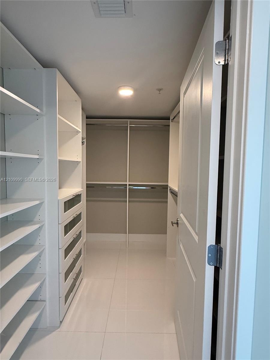 Walk-in closet featuring white built-in shelving, integrated dresser drawers with glass inserts, polished tile flooring, and dual-level hanging rods
