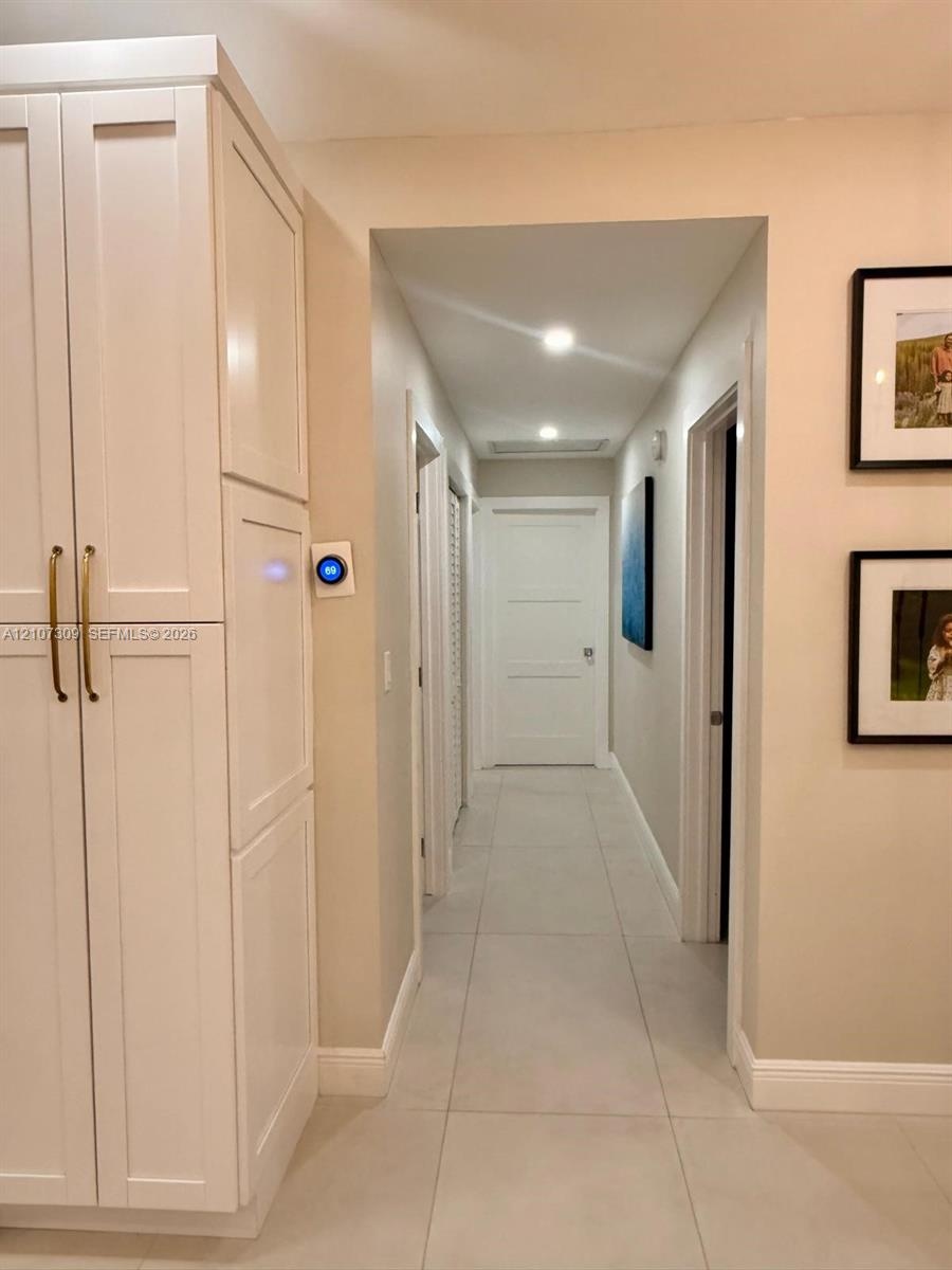 Tall, shaker-style built-in cabinetry with brass hardware, large-format neutral floor tile, recessed ceiling lighting, and a smart thermostat