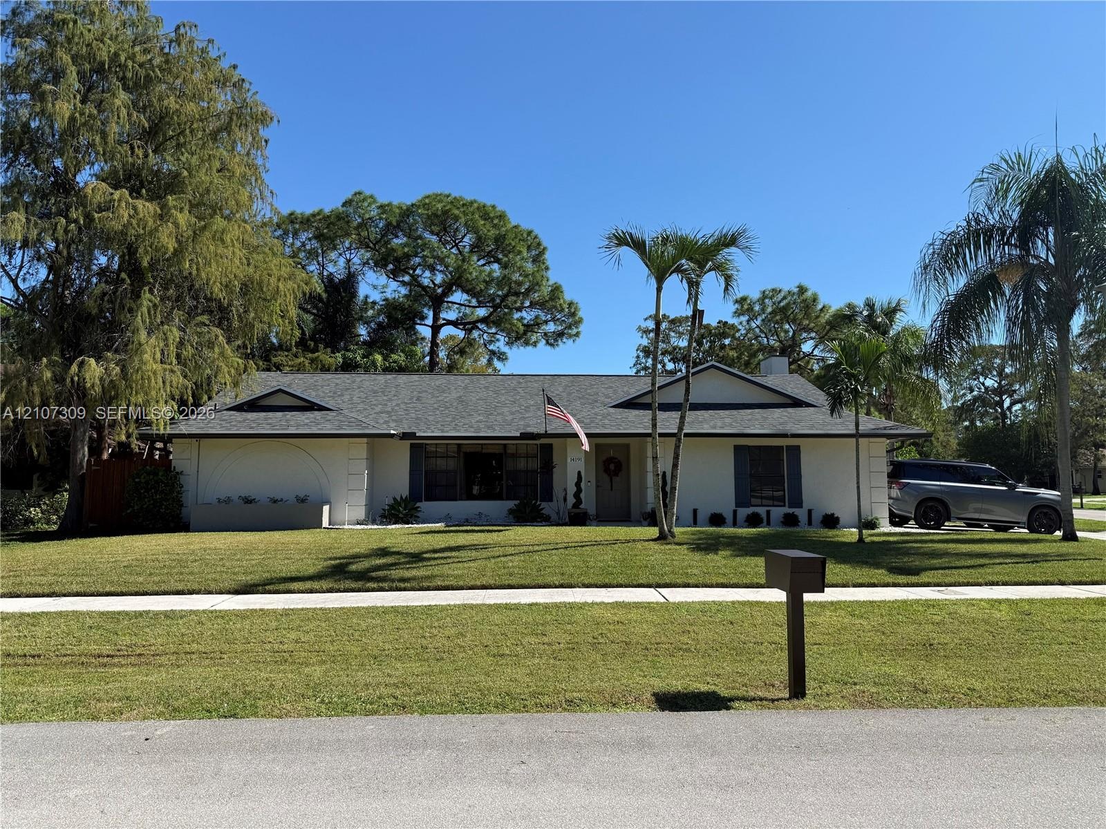 Single-story exterior featuring a light-toned stucco façade, a shingled roof, contrasting window shutters, and established palm trees
