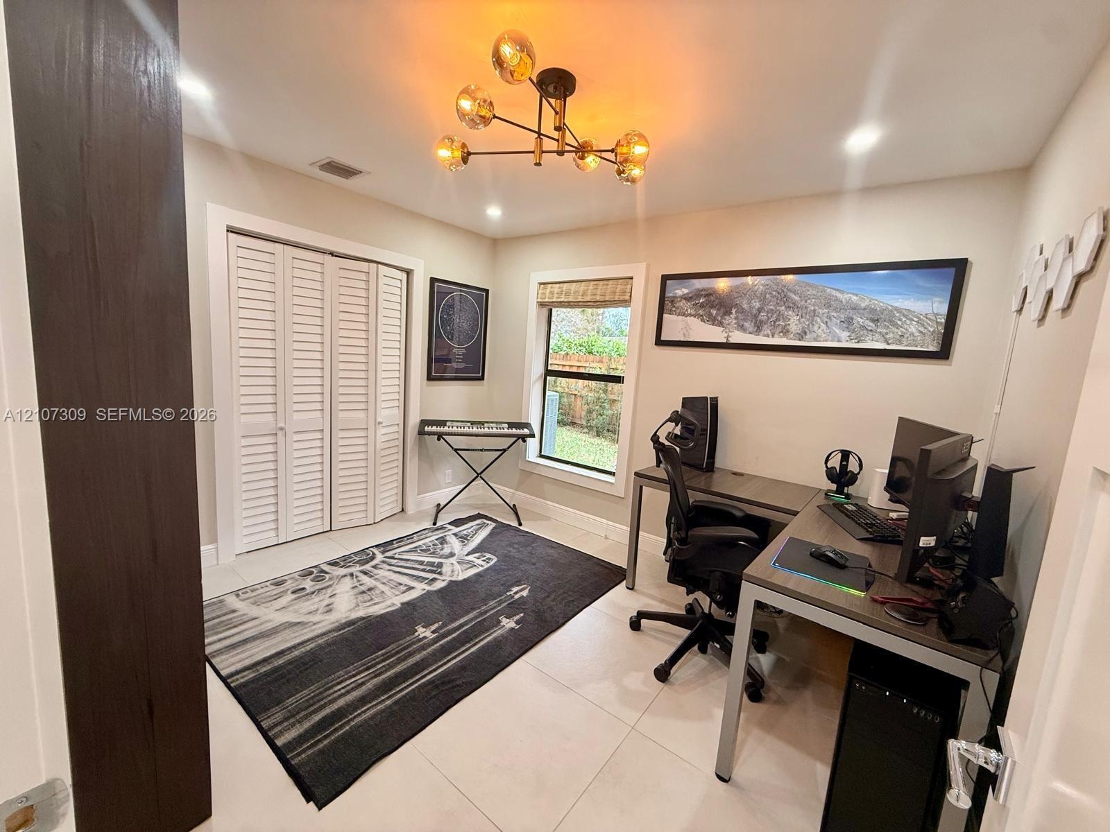 Room featuring neutral-toned tile flooring, louvered bi-fold closet doors, a multi-arm sputnik-style light fixture, and a window with a woven shade