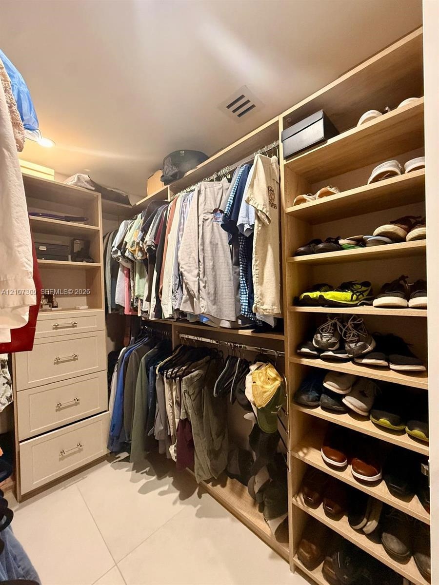 Walk-in closet featuring custom light-finish wood cabinetry, multiple tiers of hanging storage, built-in shelving for footwear, and a four-drawer dres