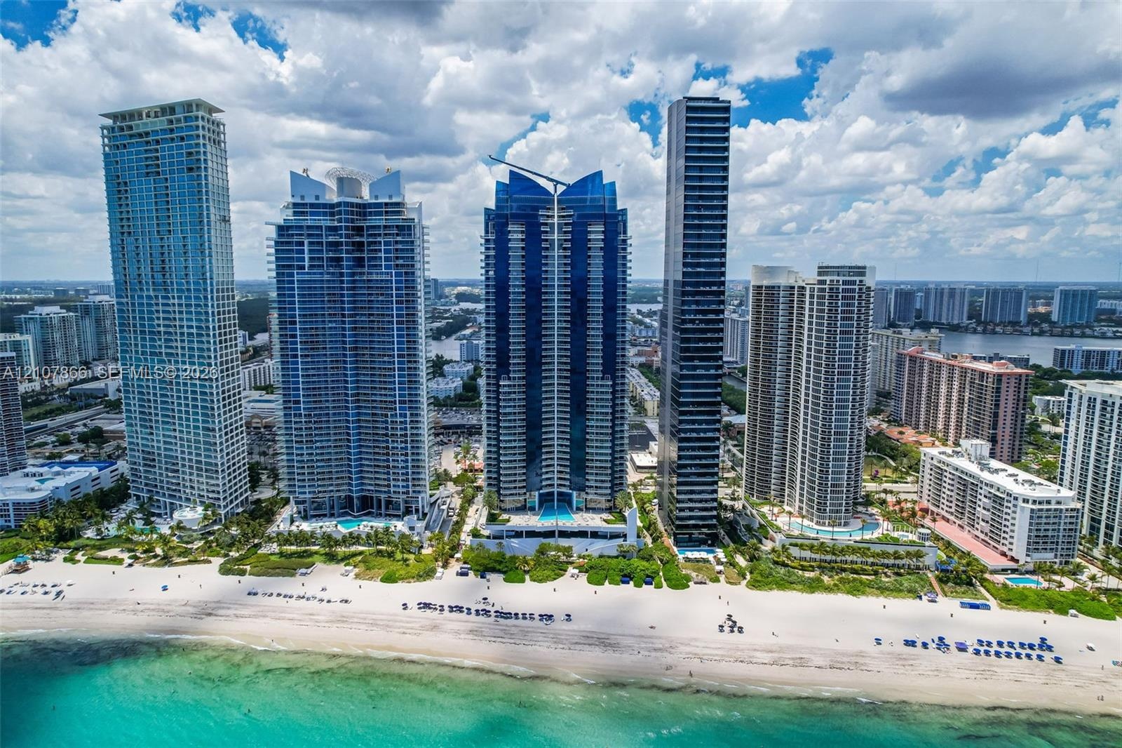 High-rise coastal development featuring glass-paneled architecture, direct oceanfront access, extensive white sand shoreline, and ground-level pool fa