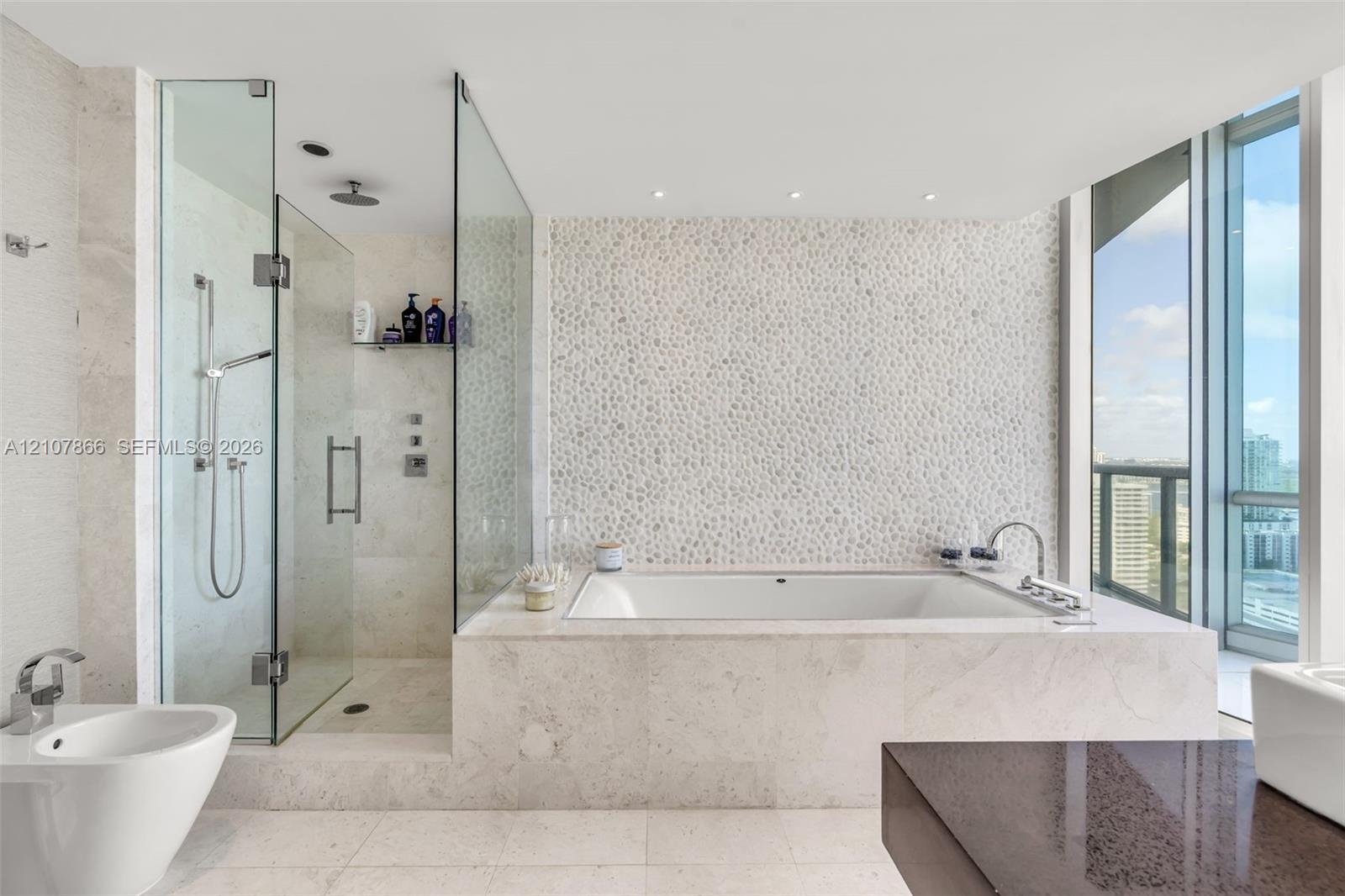 Bathroom featuring a built-in soaking tub, glass-enclosed walk-in shower with a rainfall showerhead, stone-tile flooring, textured stone-accent wall, 