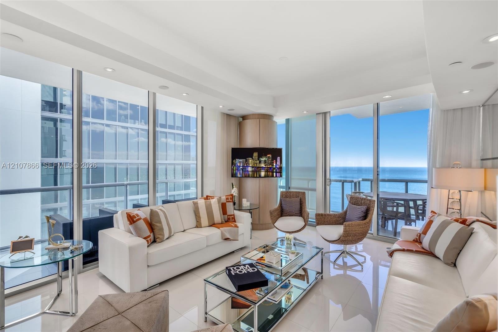 Floor-to-ceiling glass walls, polished tile flooring, recessed lighting, and a wrap-around balcony with ocean scenery