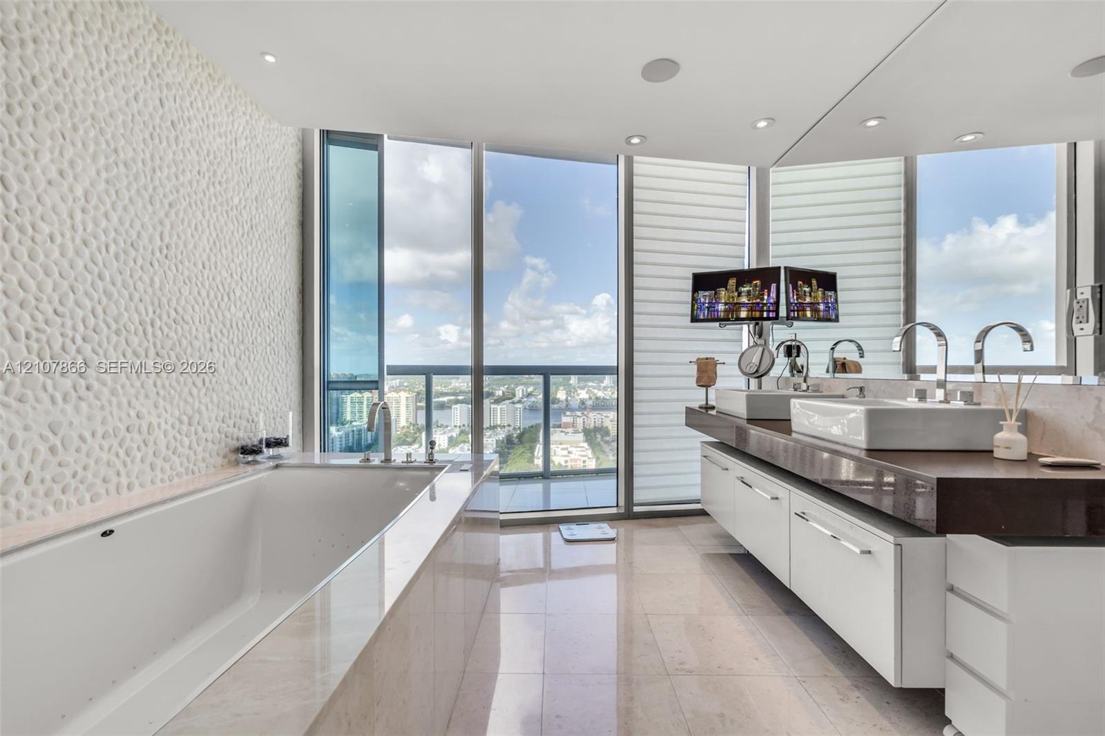 Bathroom featuring floor-to-ceiling windows, a deep soaking tub with a textured stone accent wall, a floating dual-sink vanity with a countertop, and 