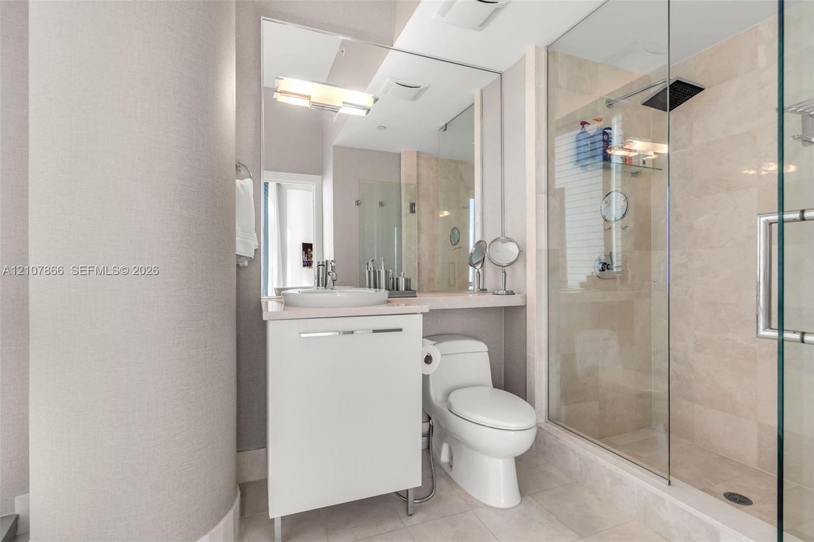 Bathroom featuring a white vanity with a vessel sink, a full-length wall mirror, a glass-enclosed walk-in shower with stone-tile surround, and a rain-
