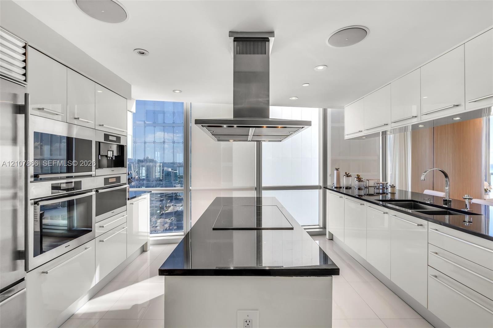 Modern kitchen featuring high-gloss white cabinetry, a center island with a dark solid-surface countertop, stainless steel integrated wall ovens, a ce