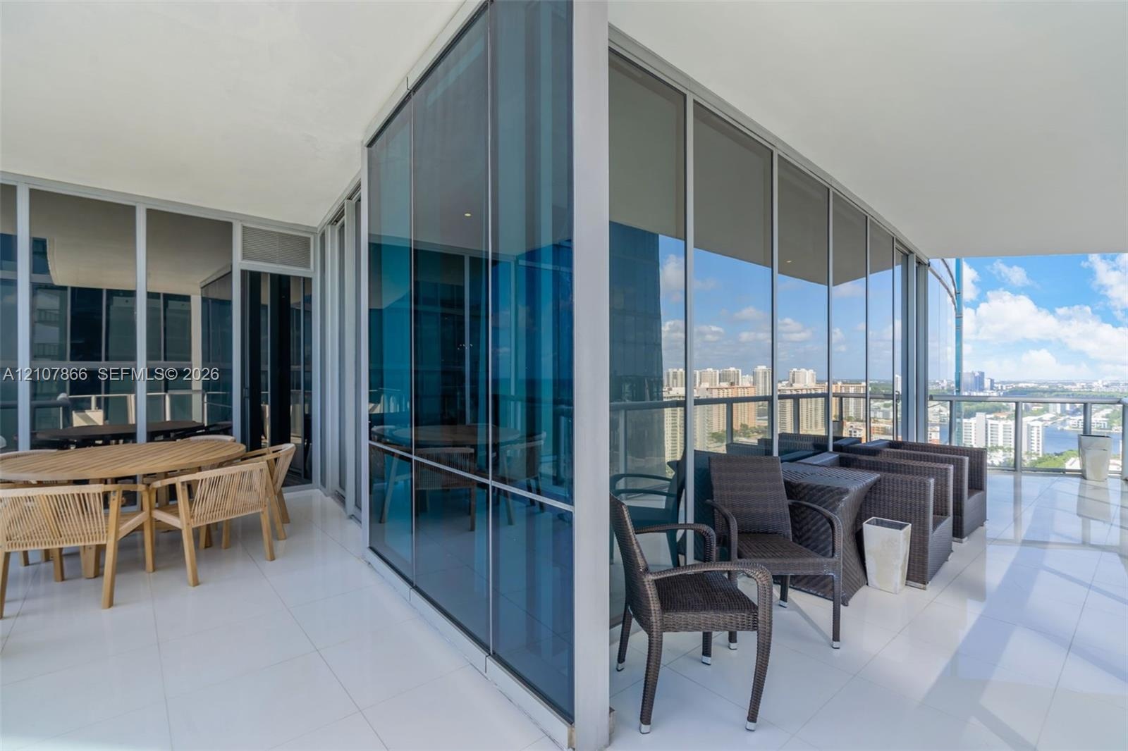 Wraparound balcony featuring floor-to-ceiling glass paneling, reflective window glazing, and large-format tile flooring