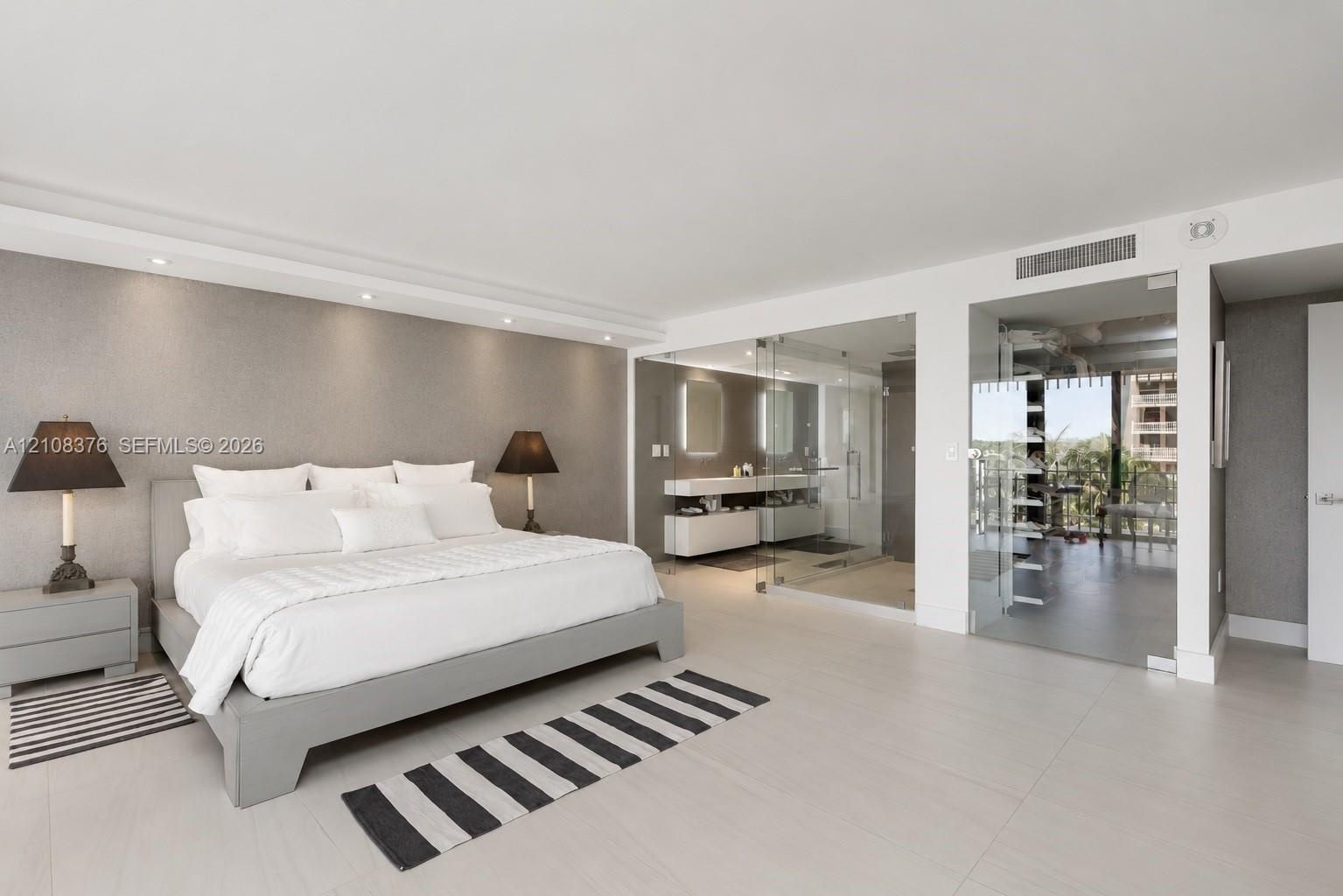 Neutral-toned interior space featuring large-format tile flooring, recessed ceiling lighting, textured accent wall, and glass-enclosed bathroom area