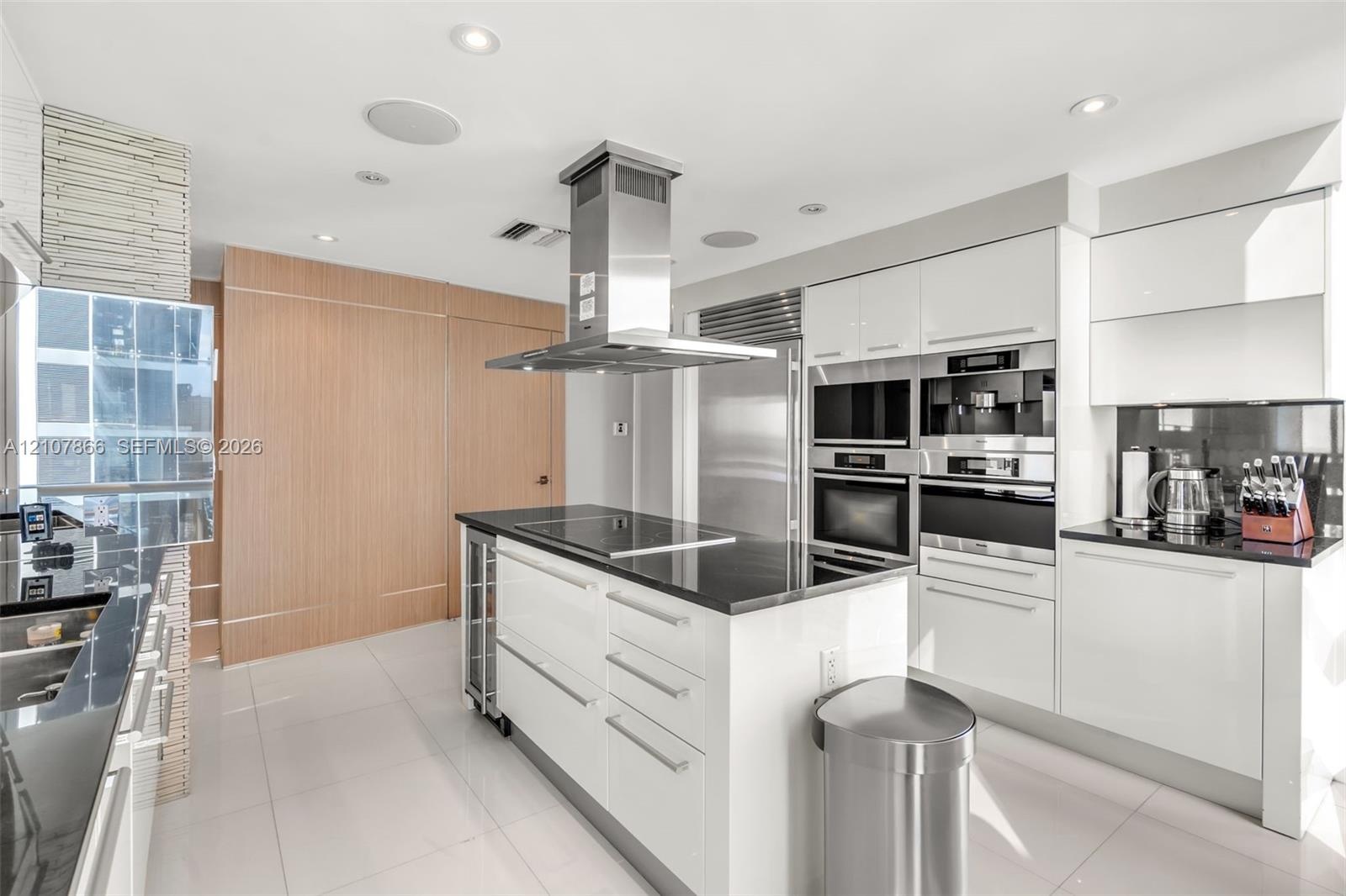 Contemporary kitchen featuring high-gloss white cabinetry, polished stone countertops, stainless steel professional-grade appliances, a central island