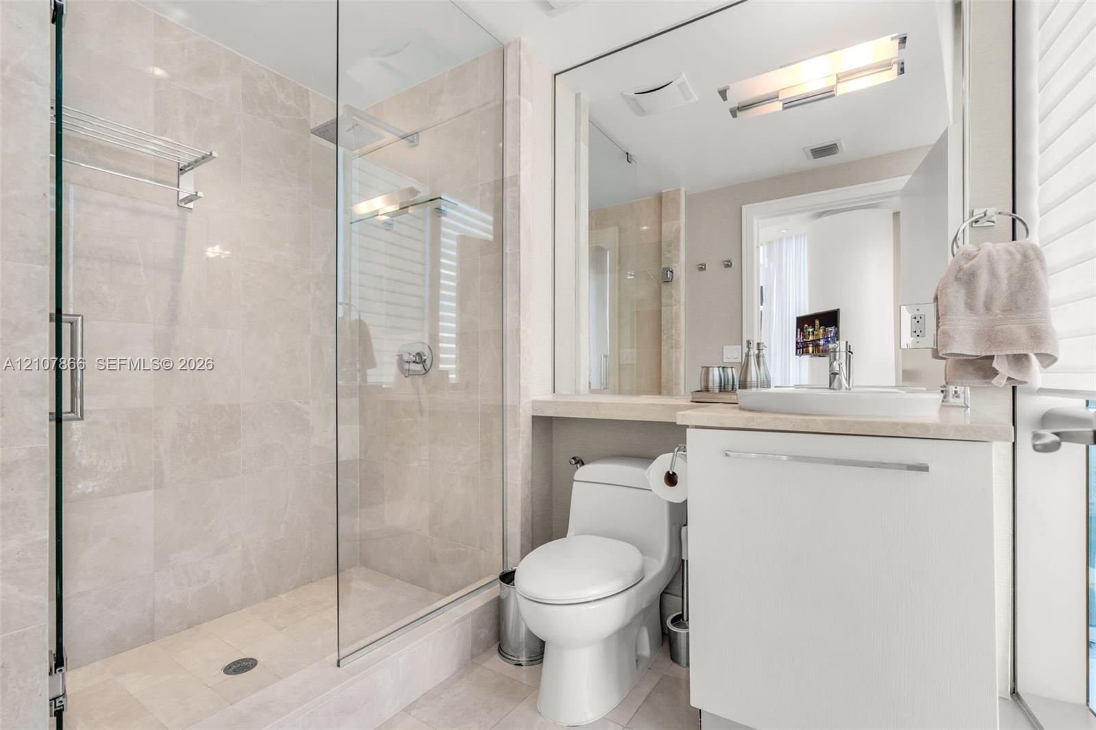 Glass-enclosed walk-in shower with tile surround, neutral-tone wall tile, white cabinetry, integrated sink, and large vanity mirror