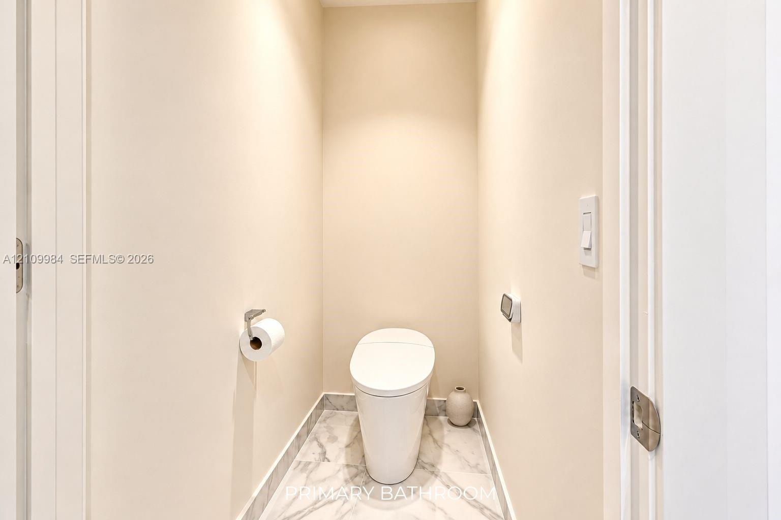 Enclosed water closet featuring a one-piece skirted toilet, large-format stone-finish floor tile, and brushed metal hardware