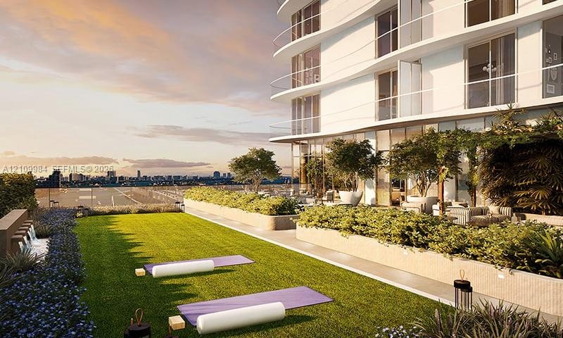 Landscaped rooftop terrace featuring synthetic turf, built-in stone planters with mature trees, glass perimeter railings, and a wall-mounted water fea